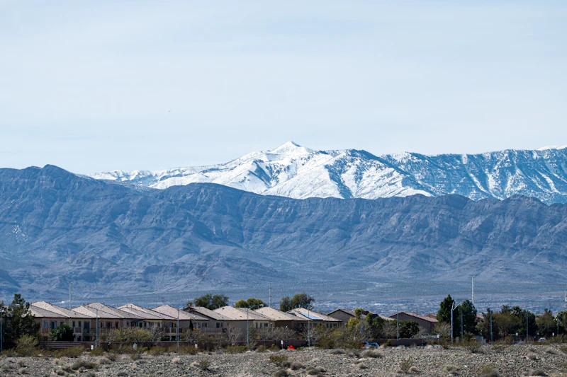 A row of tile-roofed homes at the edge of the desert, with snow-capped mountains rising behind them.